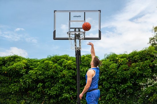 Man in blauw sporttenue gooit basketbal naar VirtuFit ring met transparant bord.