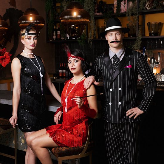 Vrouwen in 1920s-stijl outfits: zwarte jurk met pailletten en franjes, rode jurk met franjes en boa, man in gestreept pak.