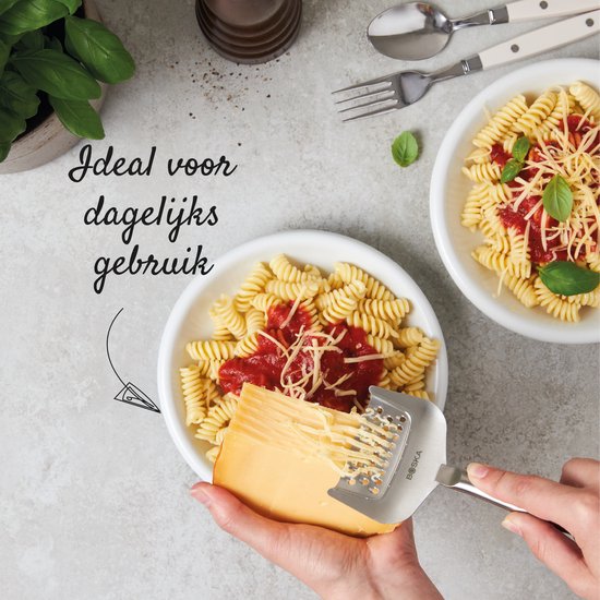 Des mains râpent un bloc de fromage avec une râpe à fromage argentée sur une assiette de pâtes avec sauce et fromage.