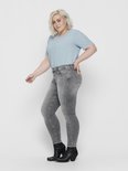 Vrouw in grijze skinny jeans met rafelende zoom en zwarte enkellaarsjes.