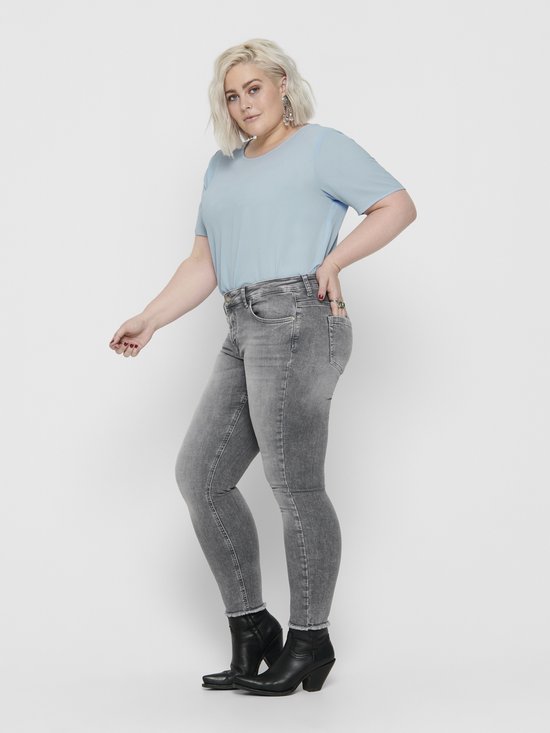 Vrouw in grijze skinny jeans met rafelende zoom en zwarte enkellaarsjes.