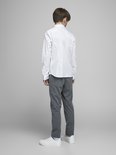 Garçon en chemise blanche à manches longues et pantalon de jogging gris, debout.