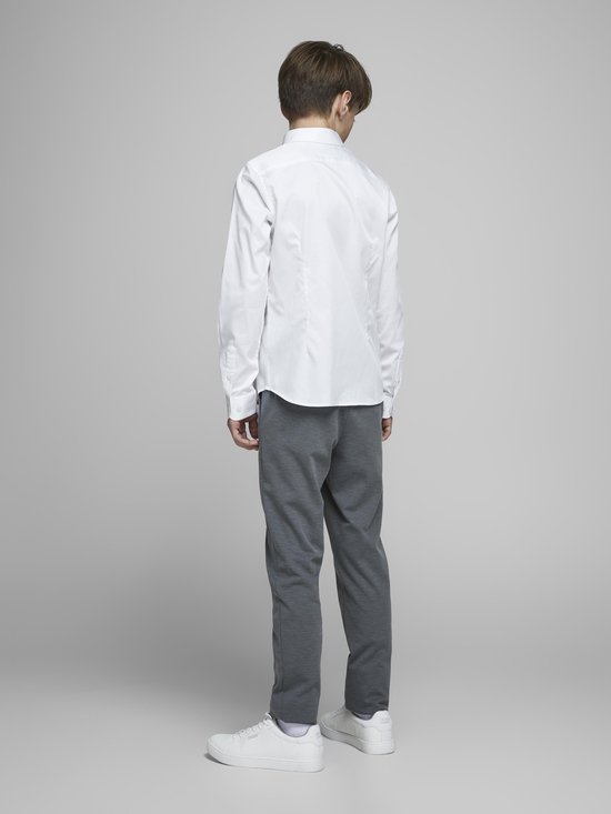 Garçon en chemise blanche à manches longues et pantalon de jogging gris, debout.