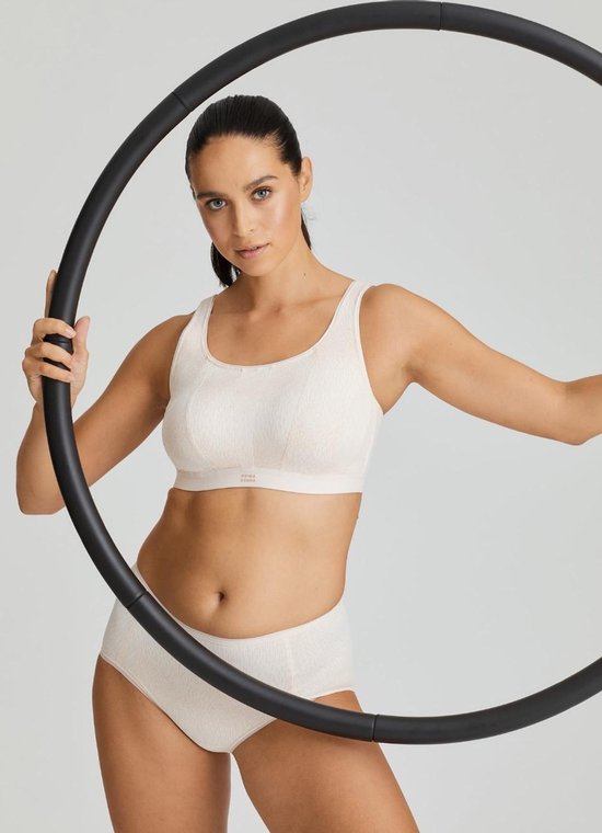 Model met lichtroze sportbeha en slip, omringd door een zwarte hoepel. Ze houdt de hoepel vast met haar handen.