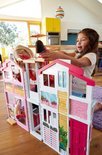 Twee kinderen spelen met een roze en wit Barbie Malibu huis met 3 verdiepingen in een woonkamer.