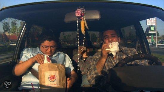 Twee mannen in een auto, één eet uit een Burger King-zak.