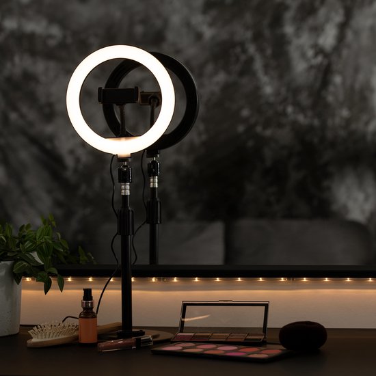 Verlichte ringlamp op een zwarte standaard met make-up accessoires op een zwarte tafel.