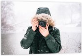 Tuinposter – Man in de Sneeuw met een Donkere Jas met een Bontkraag en een Camera - 120x80cm Foto op Tuinposter  (wanddecoratie voor buiten en binnen)