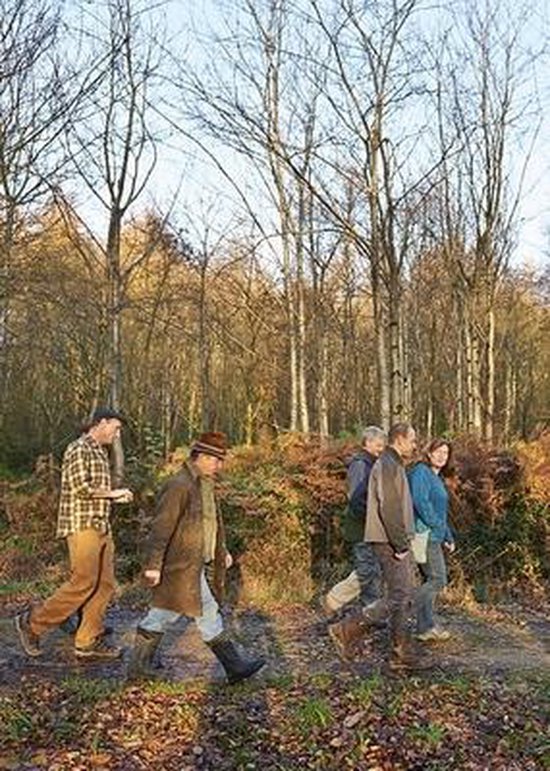 Vijf volwassenen wandelen door een bos met bruine en groene kleding, met bomen en varens op de achtergrond.