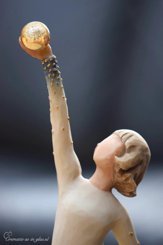 Detail van een Willow Tree beeldje, een vrouw in een witte jurk met gouden stippen die een gouden bol omhoog houdt.