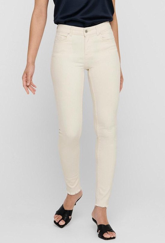 Model in crème skinny jeans met rafels aan de onderkant en zwarte sandalen.