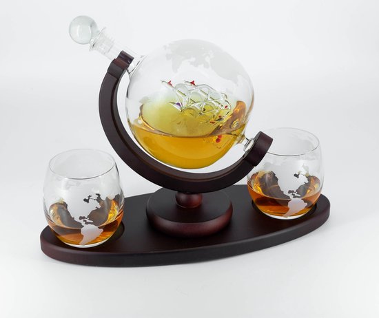 Glazen wereldbol karaf met schip in het midden, gevuld met amberkleurige drank, op houten standaard met 2 glazen.