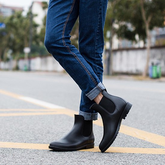 Een persoon draagt zwarte chelsea laarzen met een opgerolde jeans op straat.