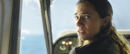 Vrouw met bruin haar kijkt bezorgd uit een vliegtuigraam naar de zee.