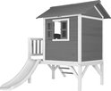 Grijze houten speelhuisje op poten met witte accenten, trap en witte glijbaan.