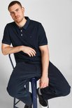 Donkerblauw poloshirt met korte mouwen en knoopjes, gedragen door een man zittend op een krukje.