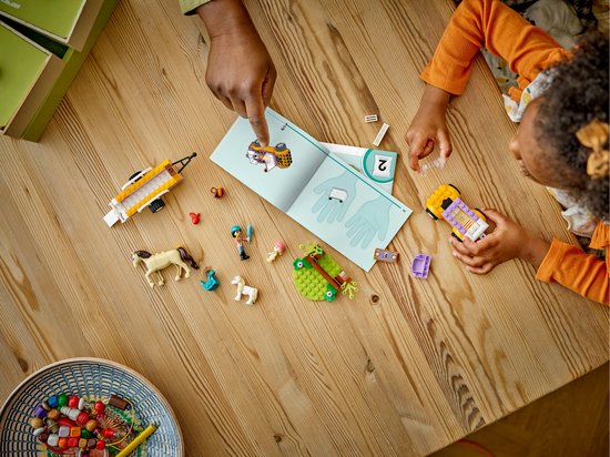 Vue de dessus de l'ensemble de remorque à chevaux LEGO Friends avec un livre et des pièces sur une table en bois.