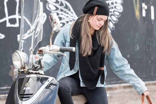 Jonge vrouw met zwarte gebreide muts en sjaal, op een scooter.