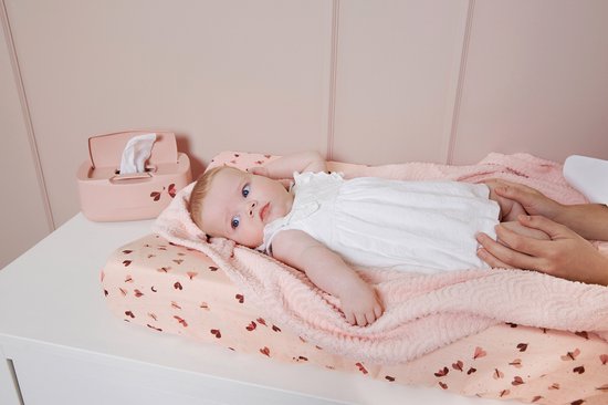 Baby met blauwe ogen, liggend op een roze aankleedkussen met vlinderprint. Een witte jurk draagt de baby.