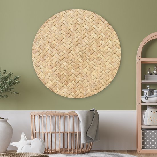 Décoration murale ronde en rotin avec motif tressé, au-dessus d'un berceau en bois dans une chambre d'enfant verte.