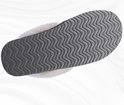 Zool van een grijze pantoffel met witte pluche voering, met golvend anti-slip profiel.