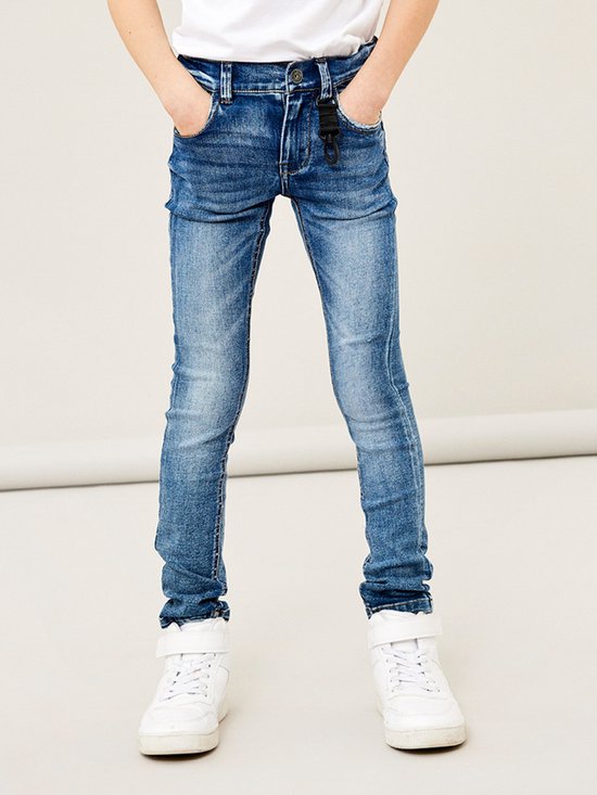 Jongens skinny jeans in medium blue denim met slijtageplekken en een zwarte sleutelhanger aan de riem.