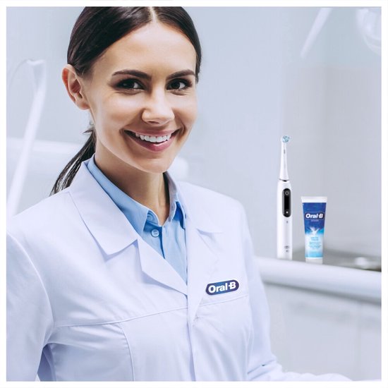 Vrouw in witte doktersjas lacht en toont een Oral-B elektrische tandenborstel en tube tandpasta.