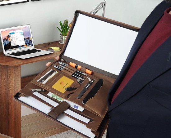 Man in pak met bruine leren map, open met documenten, pennen en laptop op bureau.