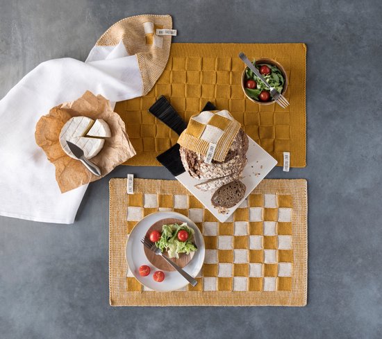Gele gebreide deken en placemat met vierkante patronen, naast een witte theedoek.