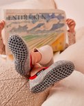 Kinderen met grijze FALKE pantoffels met rode accenten en antislip zolen lezen een krant.