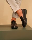 Une femme porte un mocassin marron et des collants orange, avec un pantalon gris retroussé.