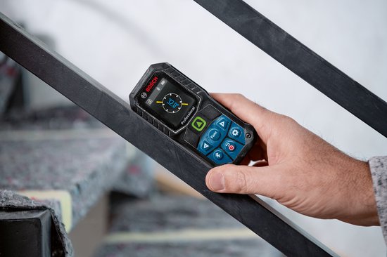Hand houdt Bosch laser afstandmeter vast tegen een metalen leuning. Het apparaat heeft een zwart met blauw design.