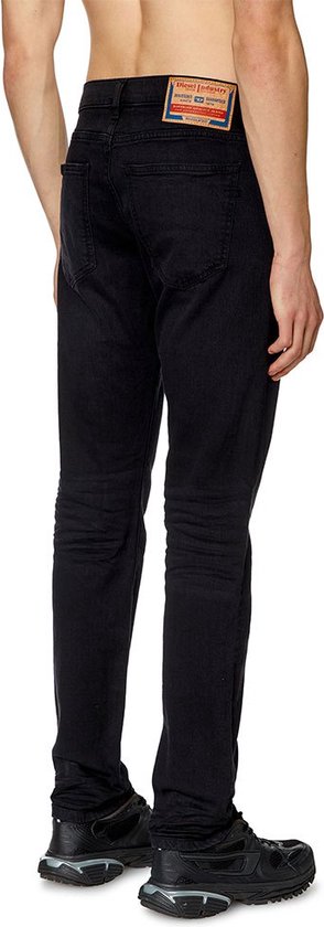 Man in zwarte jeans, van achteren gezien. De broek heeft een label op de achterkant.