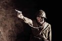 Soldaat met helm en pistool, gericht. Militair uniform met bandelier.