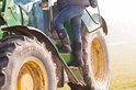 Een persoon in spijkerbroek en zwarte laarzen stapt op een grote groene tractor.