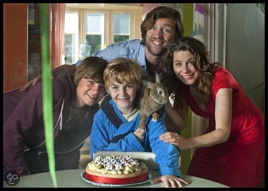 Een gezin met twee jongens, een jongen met een konijn op zijn schouder, lacht naar de camera bij een verjaardagstaart.