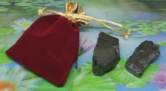 Twee ruwe, glanzende zwarte shungiet brokken naast een rood fluwelen zakje.