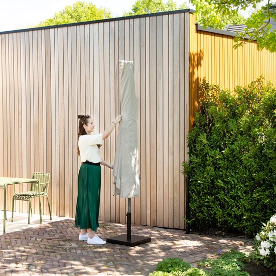 Een vrouw bedekt een opgevouwen, lichtgrijze parasol met een beschermhoes.