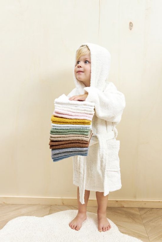 Petit garçon blond en peignoir blanc tenant une pile de serviettes multicolores.