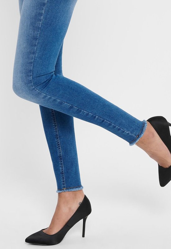 Blauwe skinny jeans met rafelige zoom, gedragen met zwarte pumps.