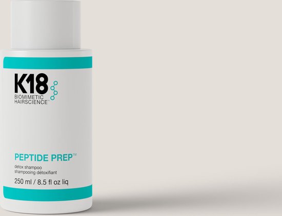 Witte K18 Peptide Prep Detox Shampoo fles met turquoise banden, tegen een zachte grijze achtergrond.