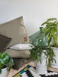 Groene kussens, een witte plaid en planten op een houten vloer met een geometrisch tapijt.