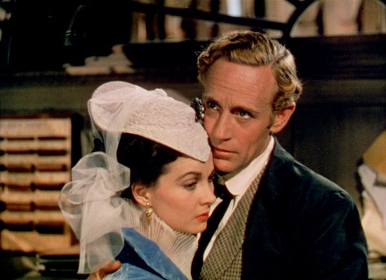 Een man omhelst Scarlett O'Hara, die een witte hoed met sluier draagt en een blauwe jurk.