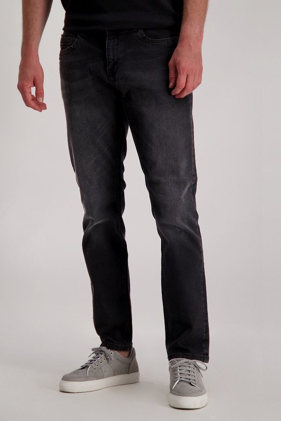 Man in een donkergrijze jeans met rechte pijpen, gedragen met grijze sneakers.