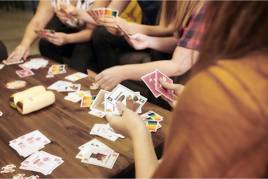 Groep vrienden speelt Throw Throw Burrito aan een tafel vol kaarten.