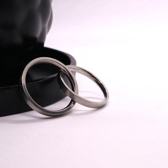 Twee zilverkleurige ringen in elkaar op een witte ondergrond.