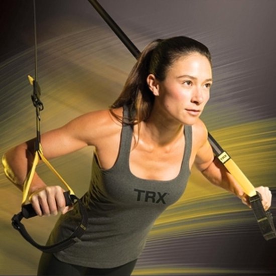 Vrouw met een staartje in een grijs TRX-shirt traint met de gele TRX-banden.