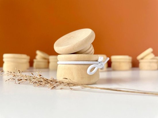 Houten bewaardoosje met schroefdop en wit koordje, met op de achtergrond meer doosjes en een gedroogd takje.