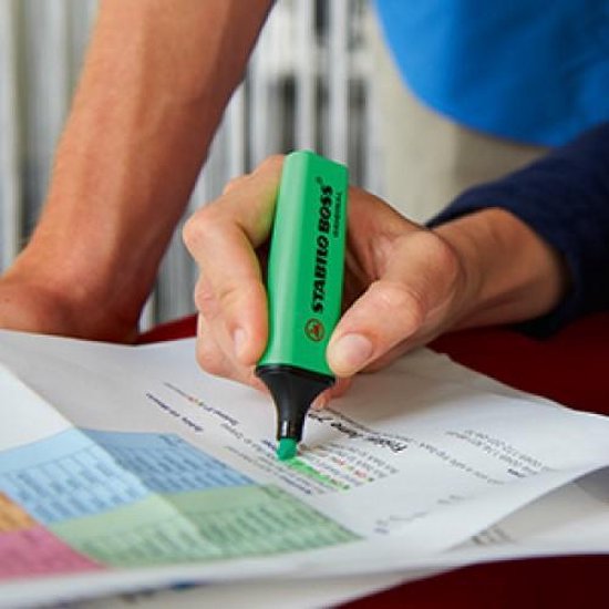 Hand met groene STABILO BOSS ORIGINAL markeerstift, markeert op papier.