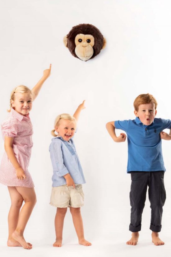 Drie kinderen die naar een aapkop wijzen die aan de muur hangt.